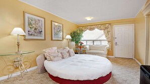 A bedroom with a large bed, a glass table, a chair, and a door. - Knights Inn Midland, ON (Midland)