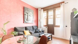 A living room with a sofa, a glass coffee table, a red chair, a Buddha statue, and a large window with curtains.