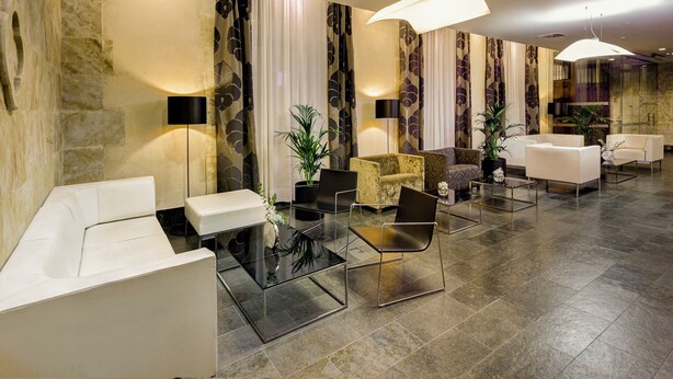 Een moderne lobby met een zithoek, een receptiebalie en een grote kroonluchter.