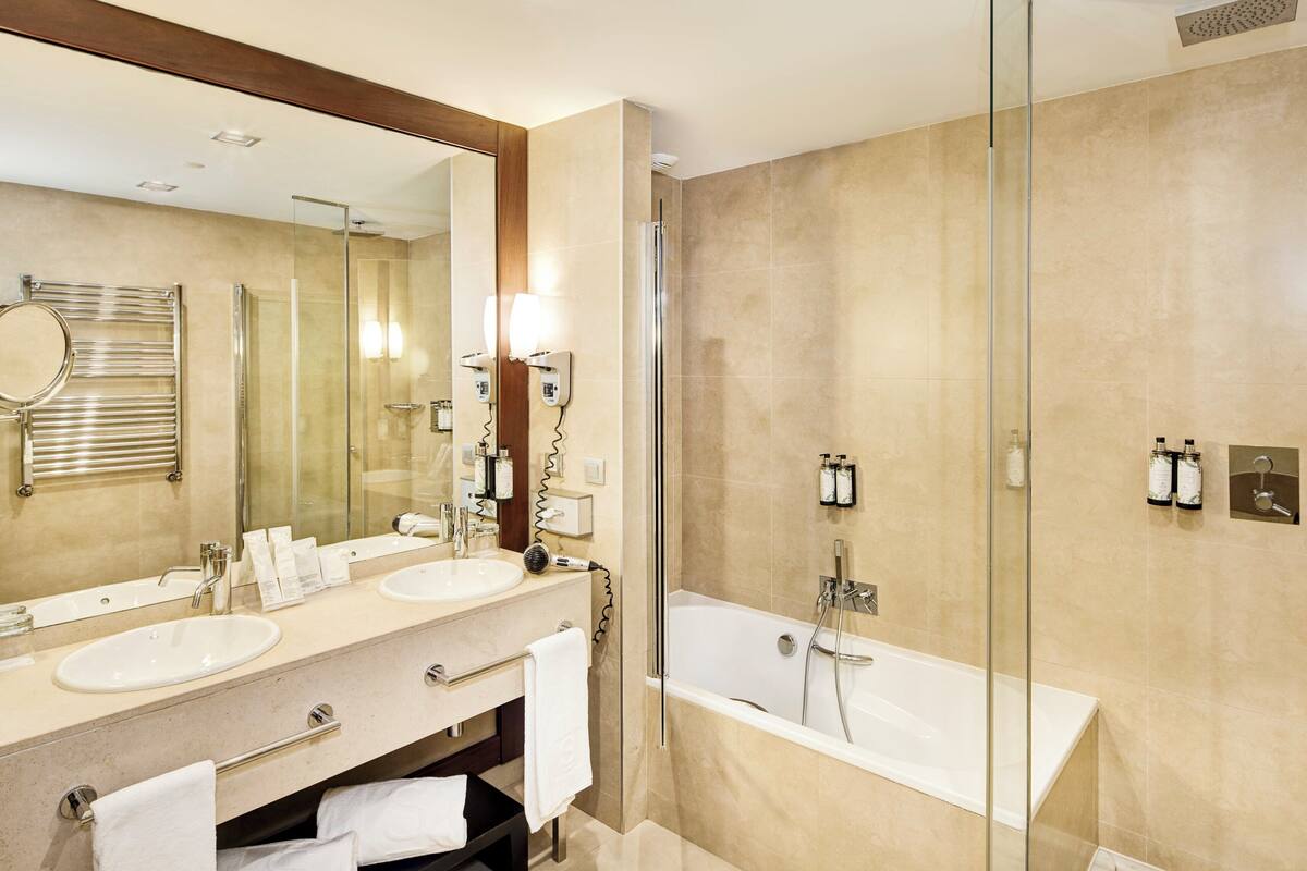 A modern bathroom with two sinks, a large mirror, a glass-enclosed shower, and a bathtub.