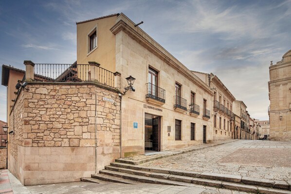 Un edificio histórico con fachada de piedra, varios balcones y una escalera que conduce a la entrada.