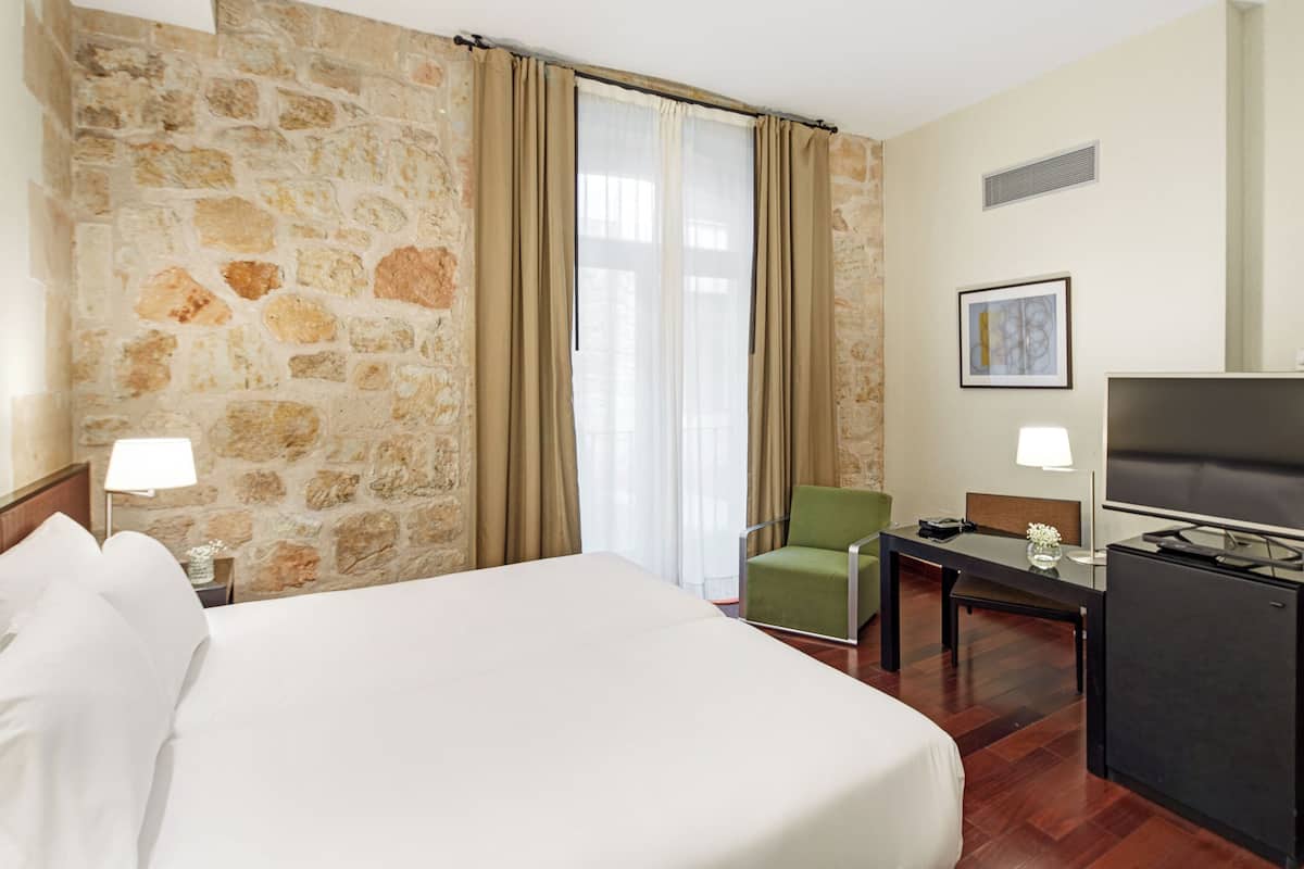 Ein Hotelzimmer mit einem großen Bett, einem Schreibtisch mit Fernseher, einem Sessel und einer Steinwand.