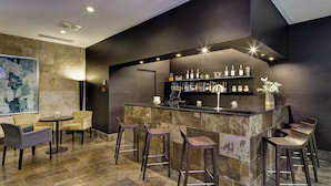 Een moderne bar met een marmeren aanrecht, barstoelen en een selectie flessen.