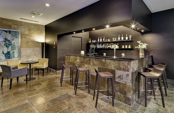 Zona de bar moderna con mostrador de mármol, taburetes y una variedad de botellas.