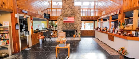 A lobby with a stone fireplace, wooden ceiling, and a reception desk with a sign for guest registration.