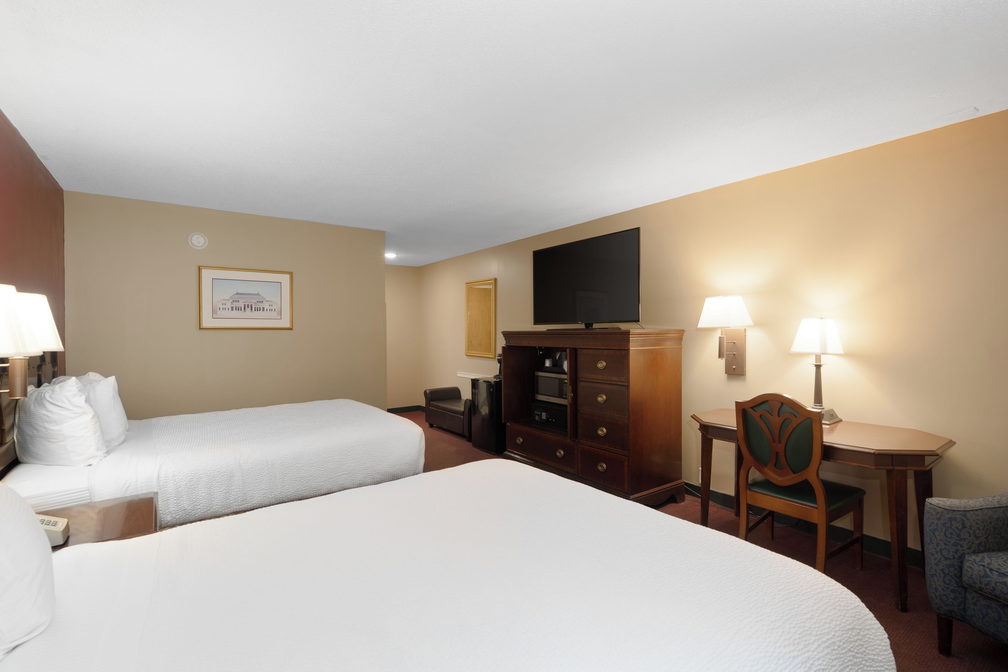 A hotel room with two beds, a TV, a desk with a chair, and a lamp.
