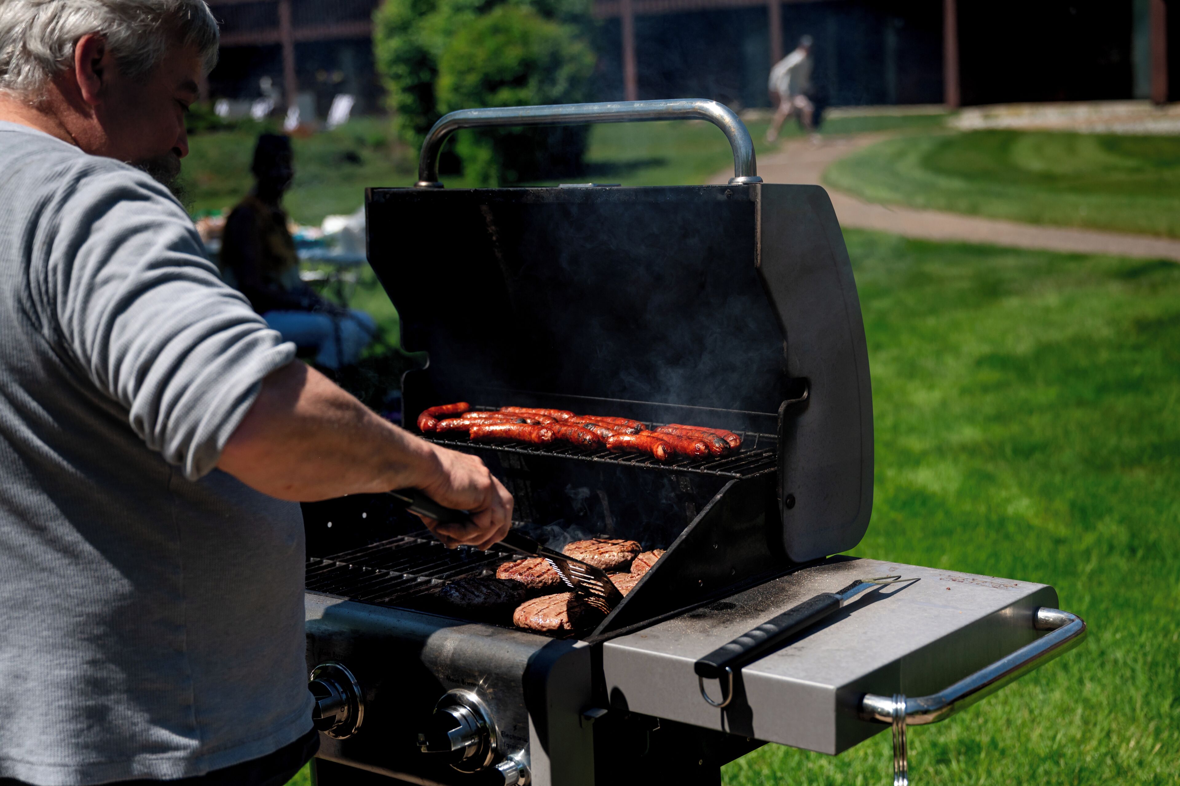A person grilling sausages and hamburgers on an outdoor grill.
