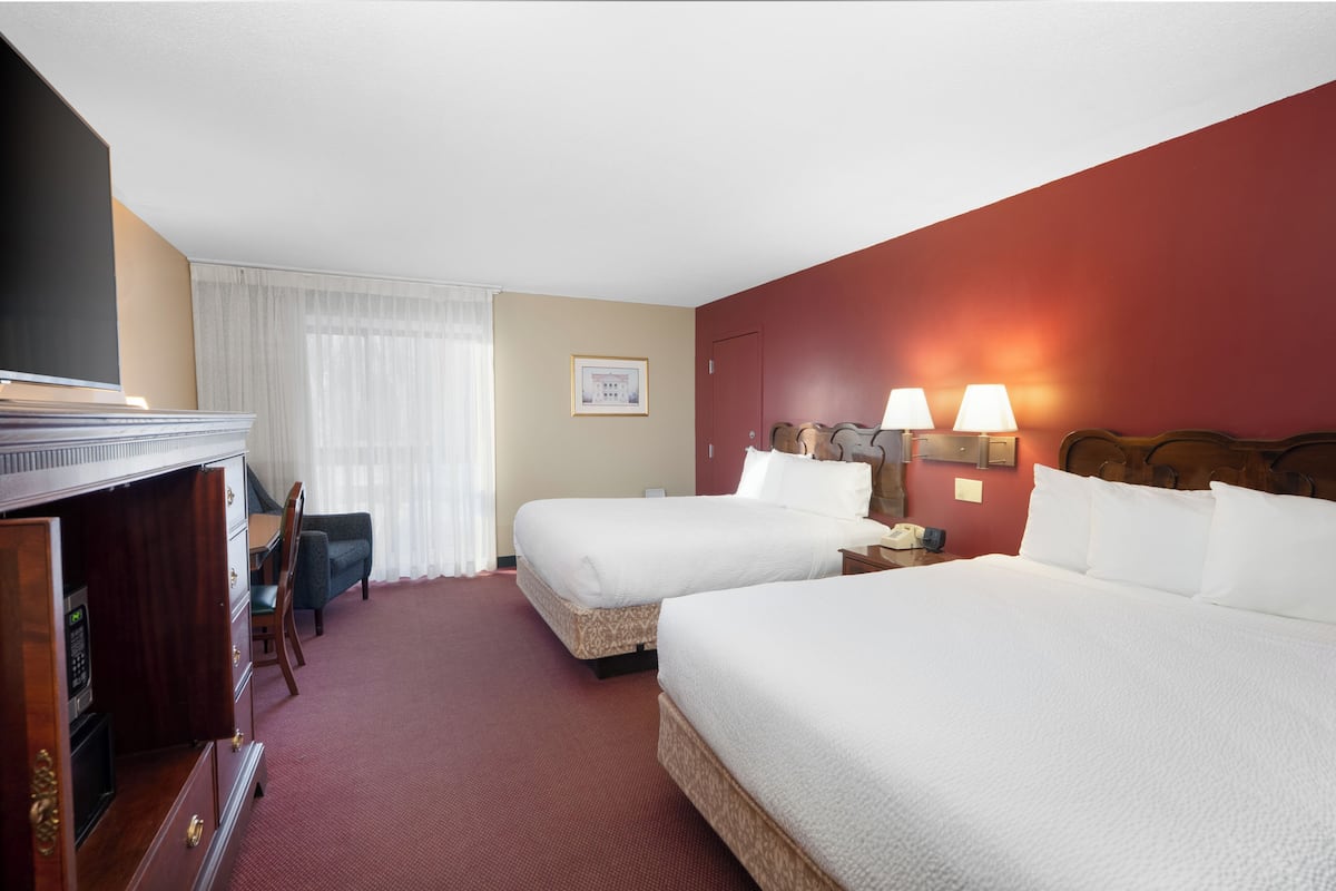 A hotel room with two beds, a desk, a chair, a TV, and a lamp.