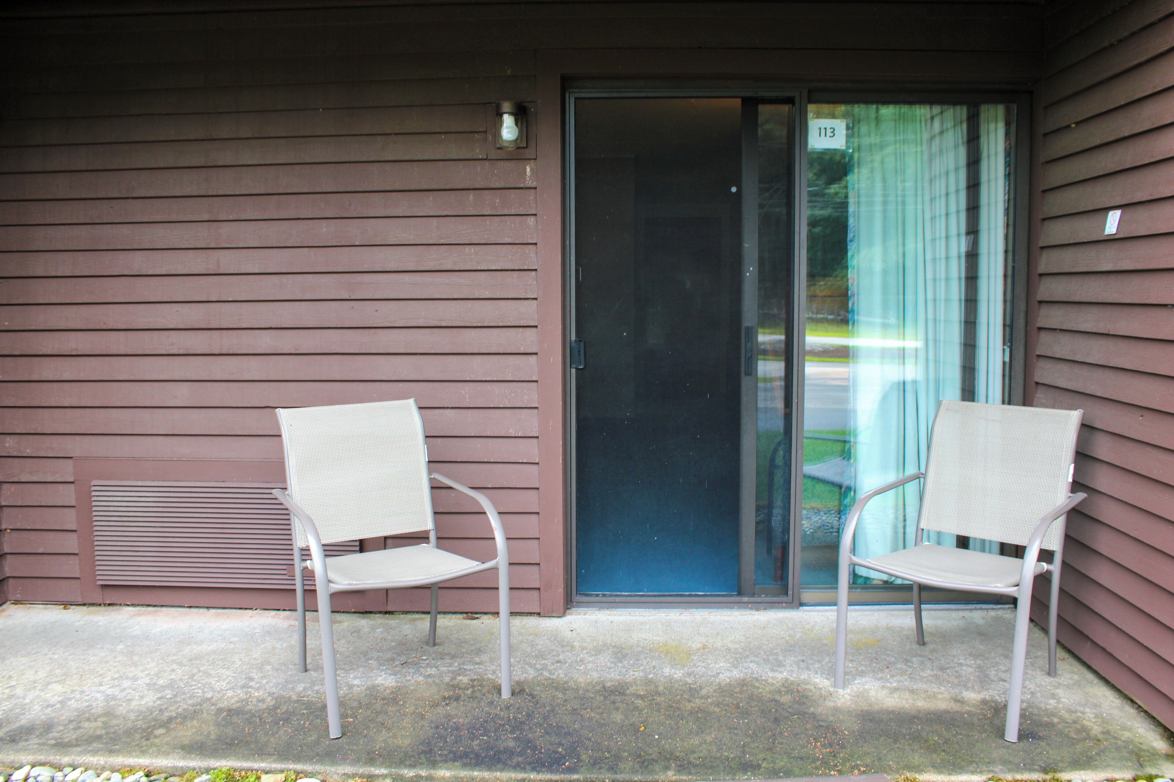 A building with two white chairs outside a sliding glass door.