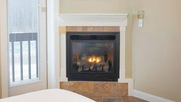 A fireplace with a stone surround, a window with blinds, and a framed picture above the fireplace.