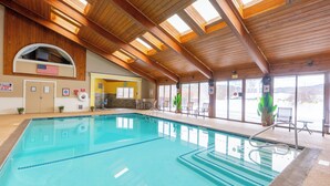 An indoor swimming pool with wooden beams, a view of the outdoors, and a flag on the wall.