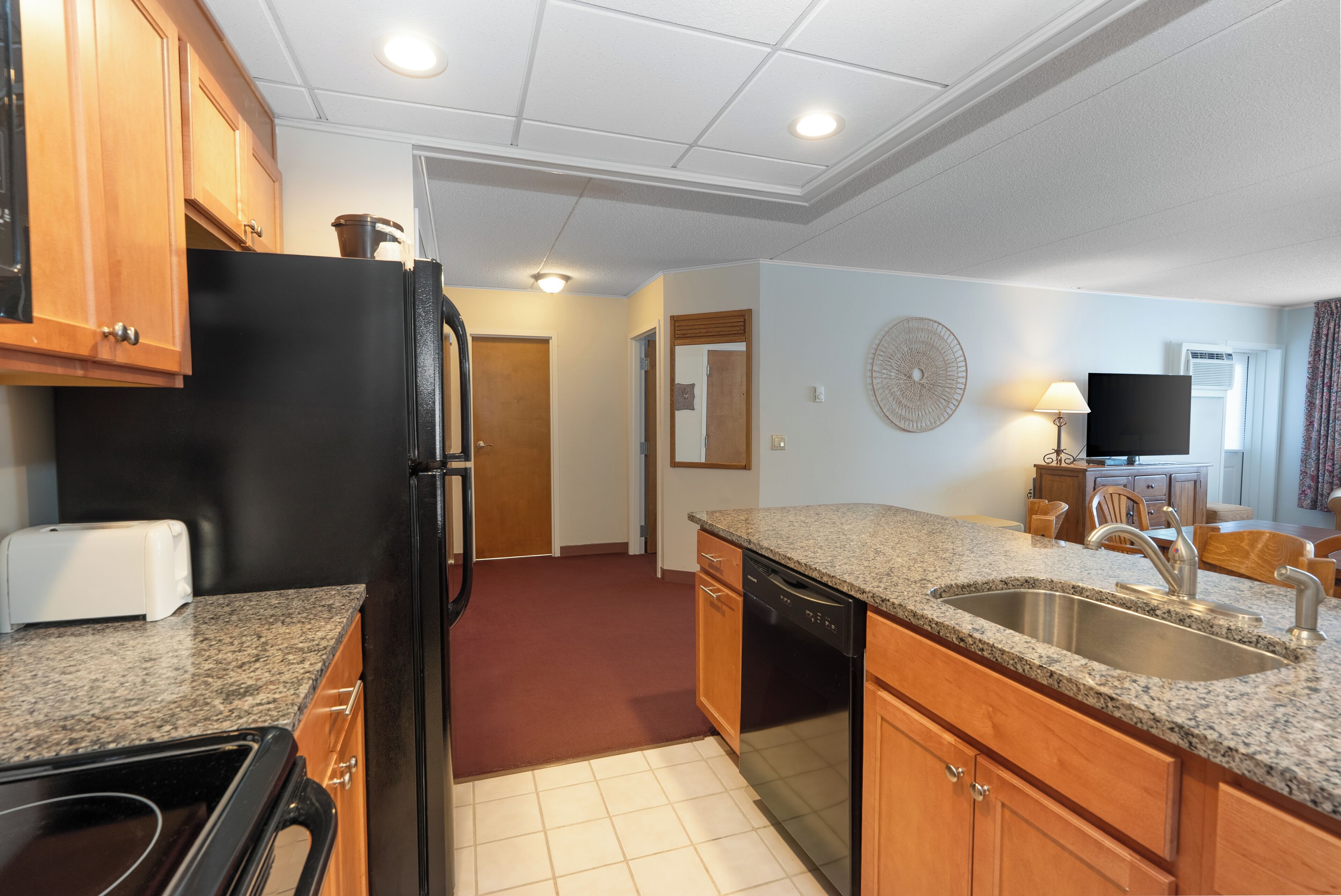 A compact kitchen with granite countertops, a black refrigerator, wooden cabinets, and a dishwasher.