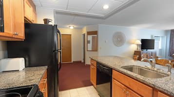A compact kitchen with granite countertops, a black refrigerator, wooden cabinets, and a dishwasher.