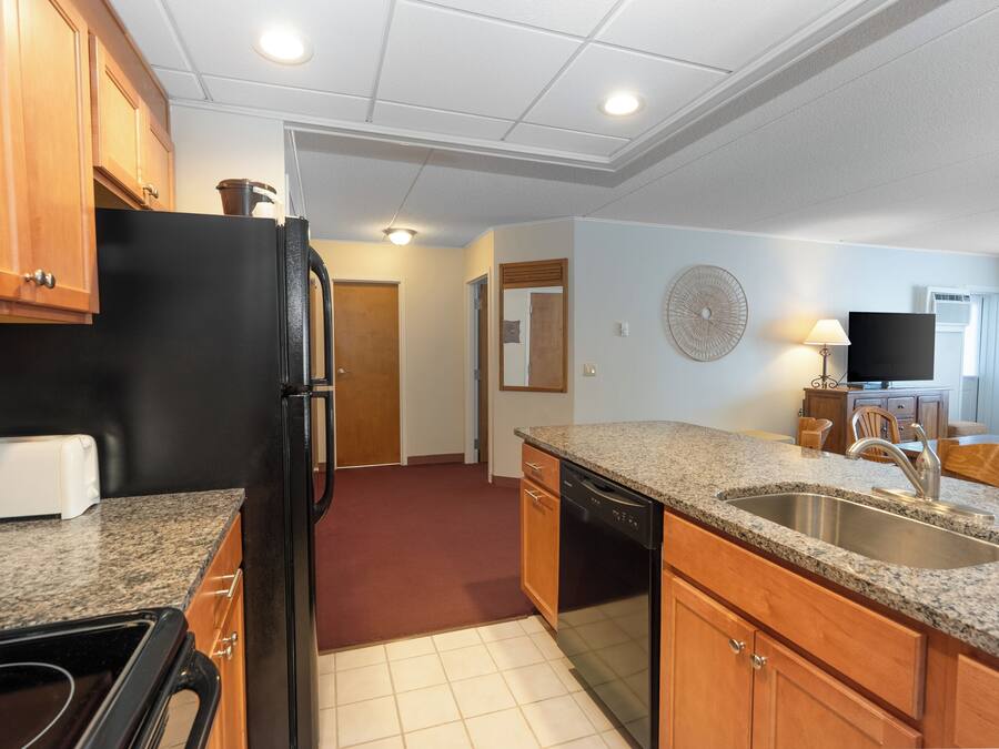 A compact kitchen with granite countertops, a black refrigerator, wooden cabinets, and a dishwasher.
