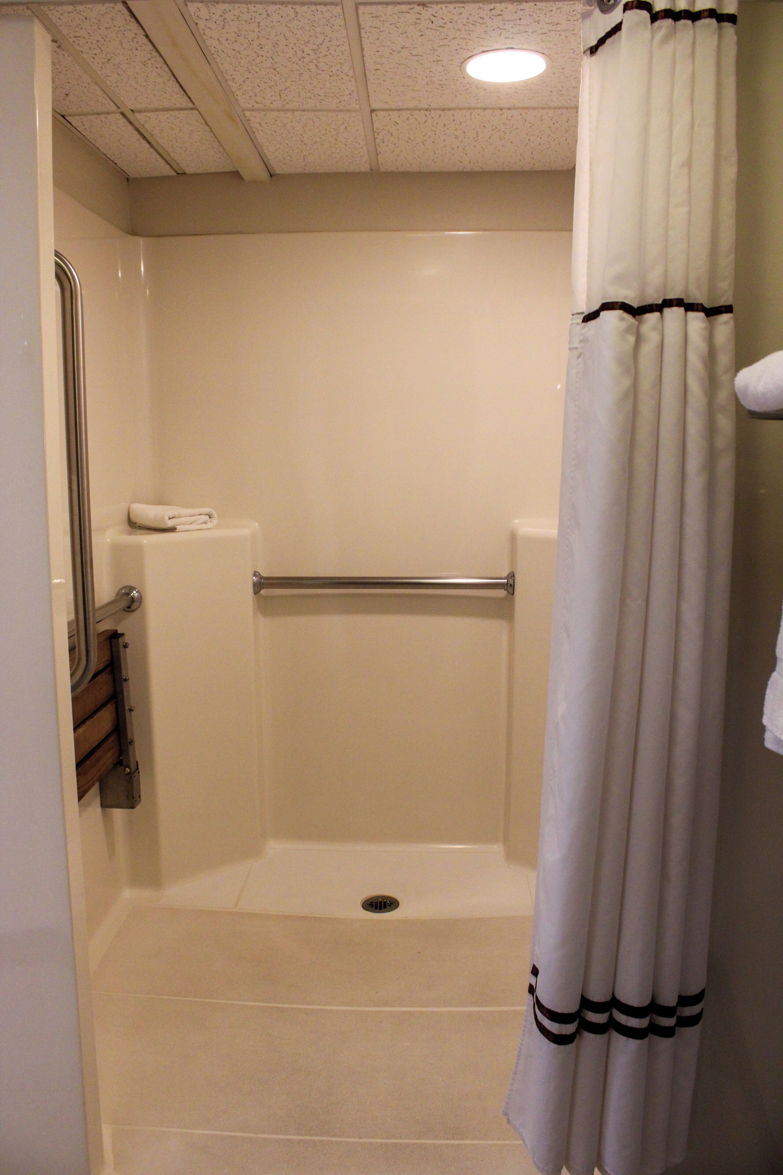 A small, enclosed shower area with a white shower curtain, a grab bar, and a towel rack.