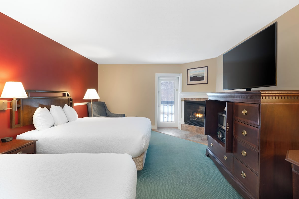 A hotel room with two beds, a television, a fireplace, and a view of the outdoors.