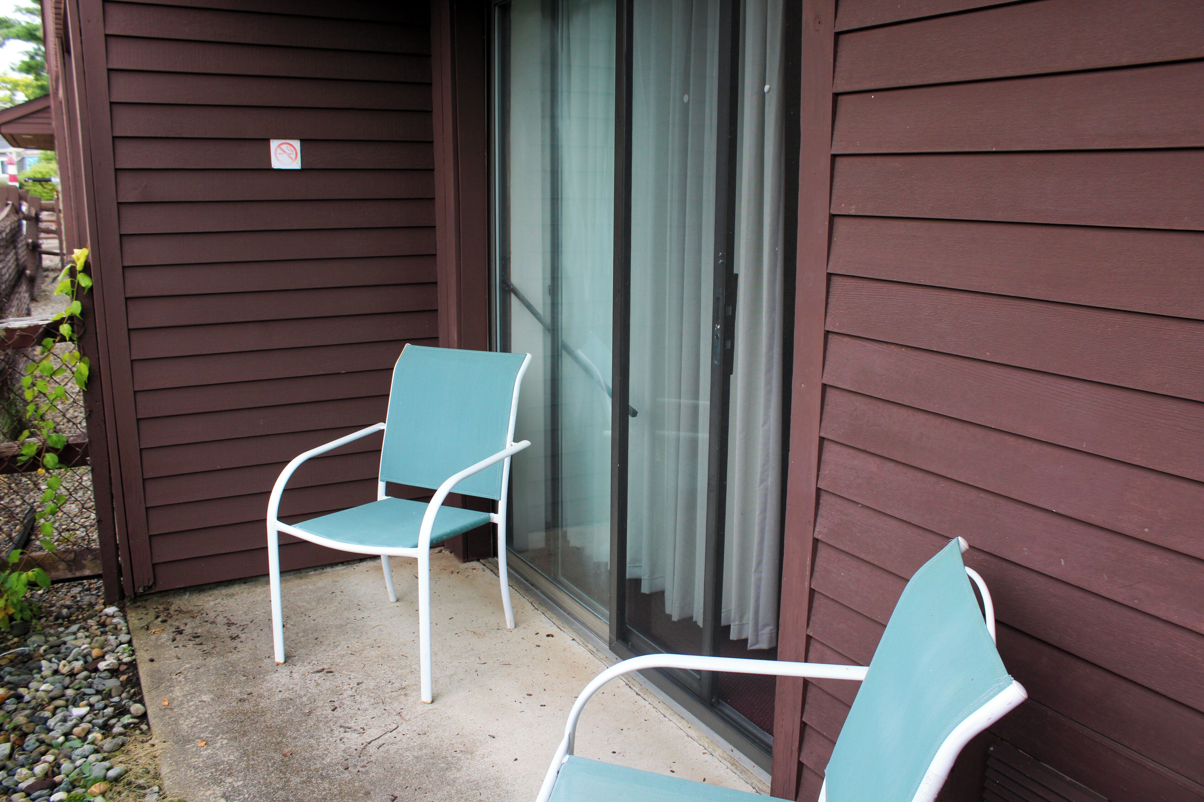 Two chairs outside a building with a sliding glass door.
