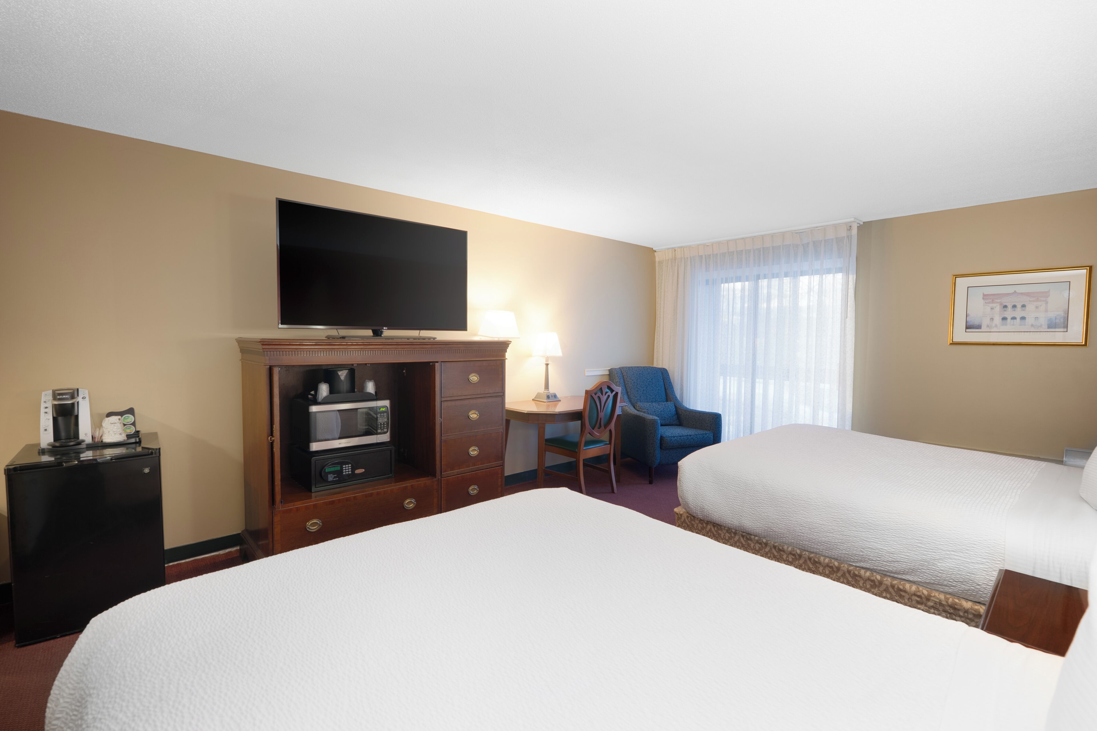 A hotel room with two beds, a TV, a desk with a lamp, a chair, and a coffee machine.
