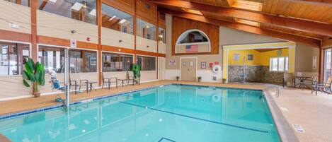 Una piscina interior con vigas de madera, una pared de piedra y vistas al piso superior.