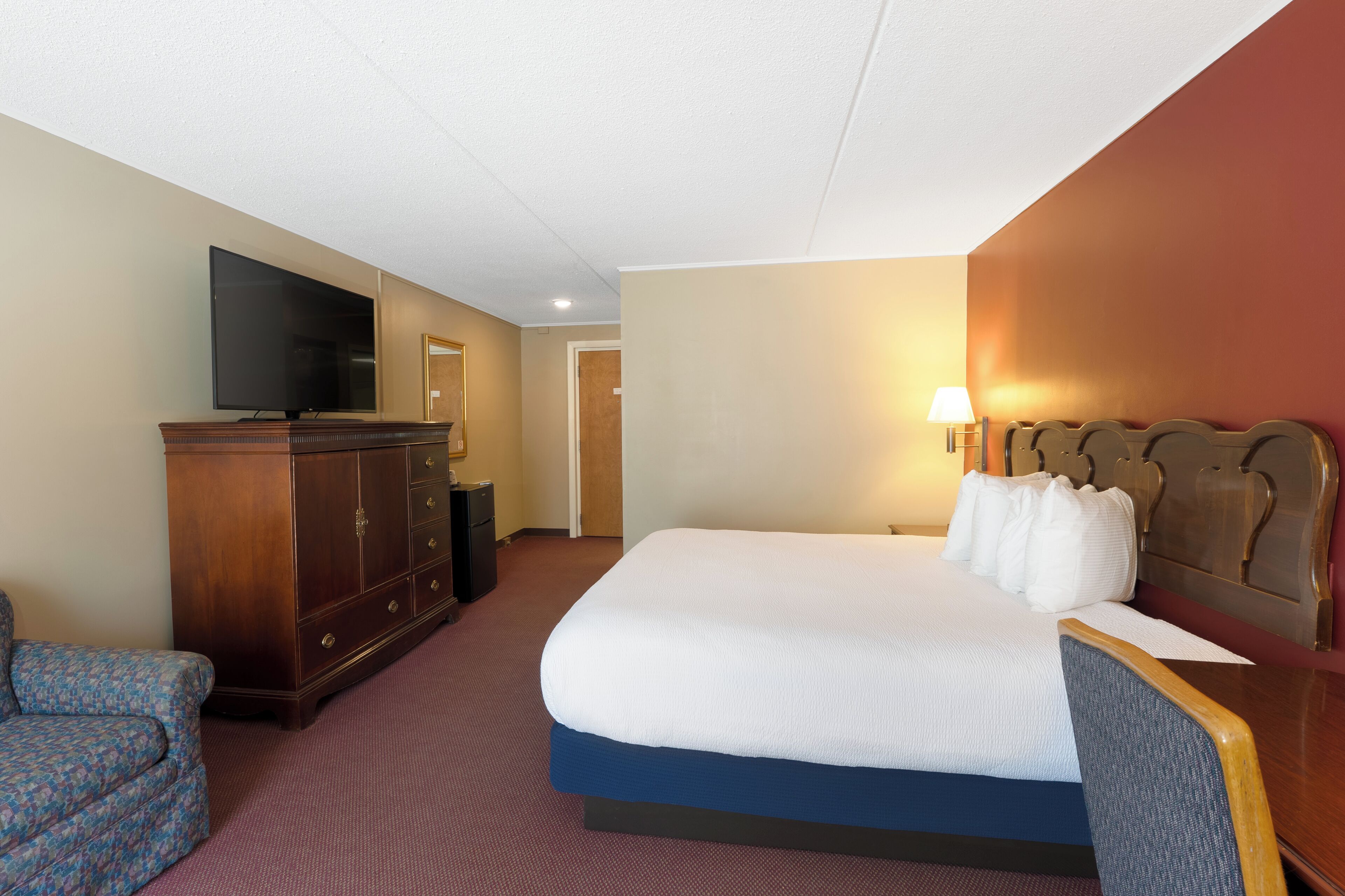 Une chambre d’hôtel avec un grand lit, une télévision, une commode en bois et une chaise.