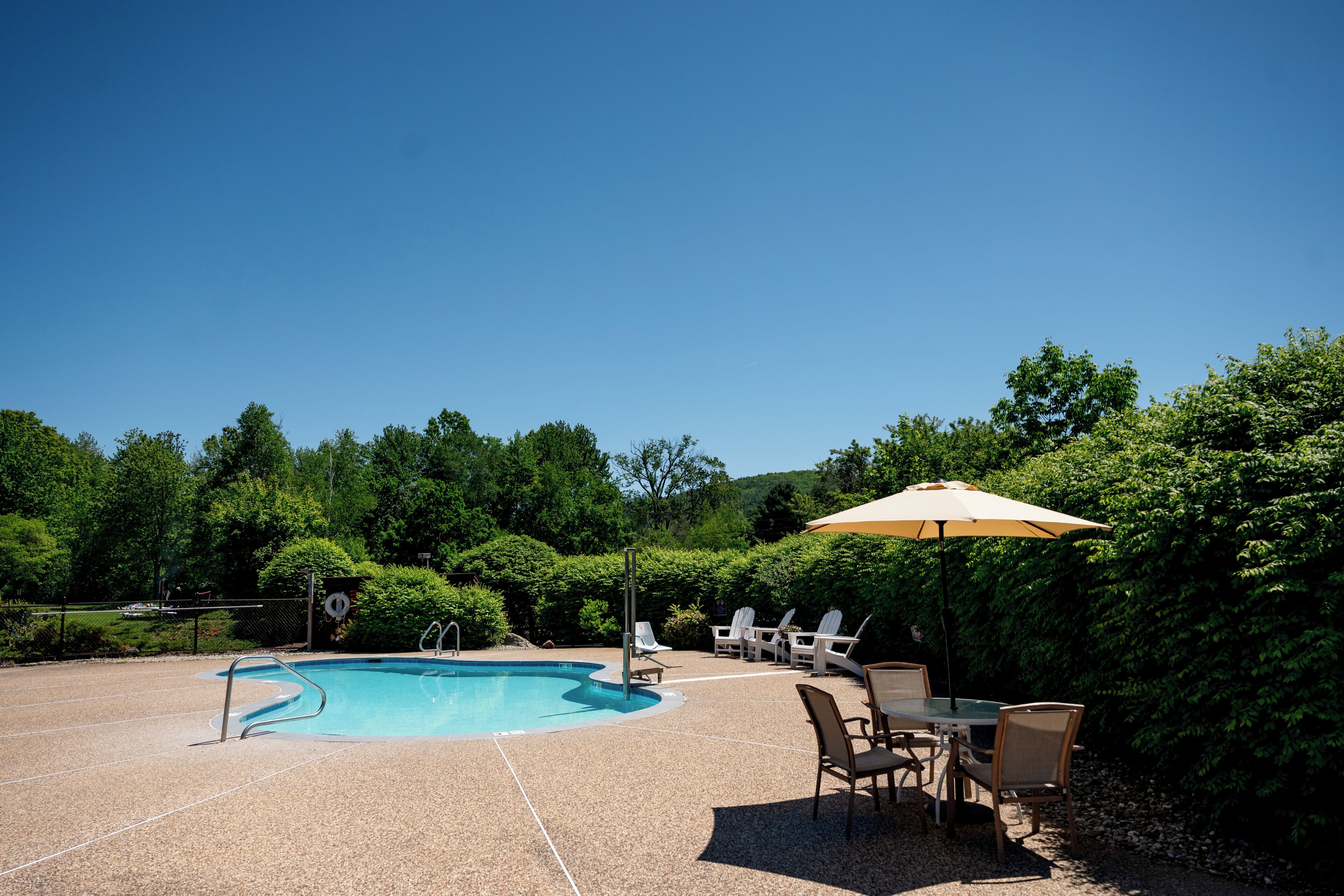 A swimming pool with a sunshade, lounge chairs, and a table.