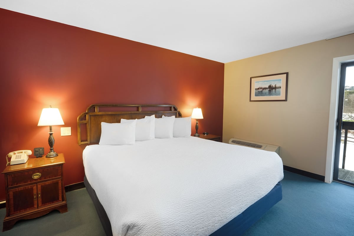 A hotel room with a large bed, two bedside lamps, a wooden nightstand, and a picture on the wall.