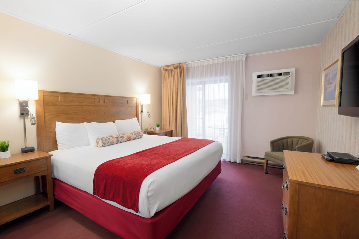 A hotel room with a large bed, a desk, a chair, a TV, and a window with curtains.
