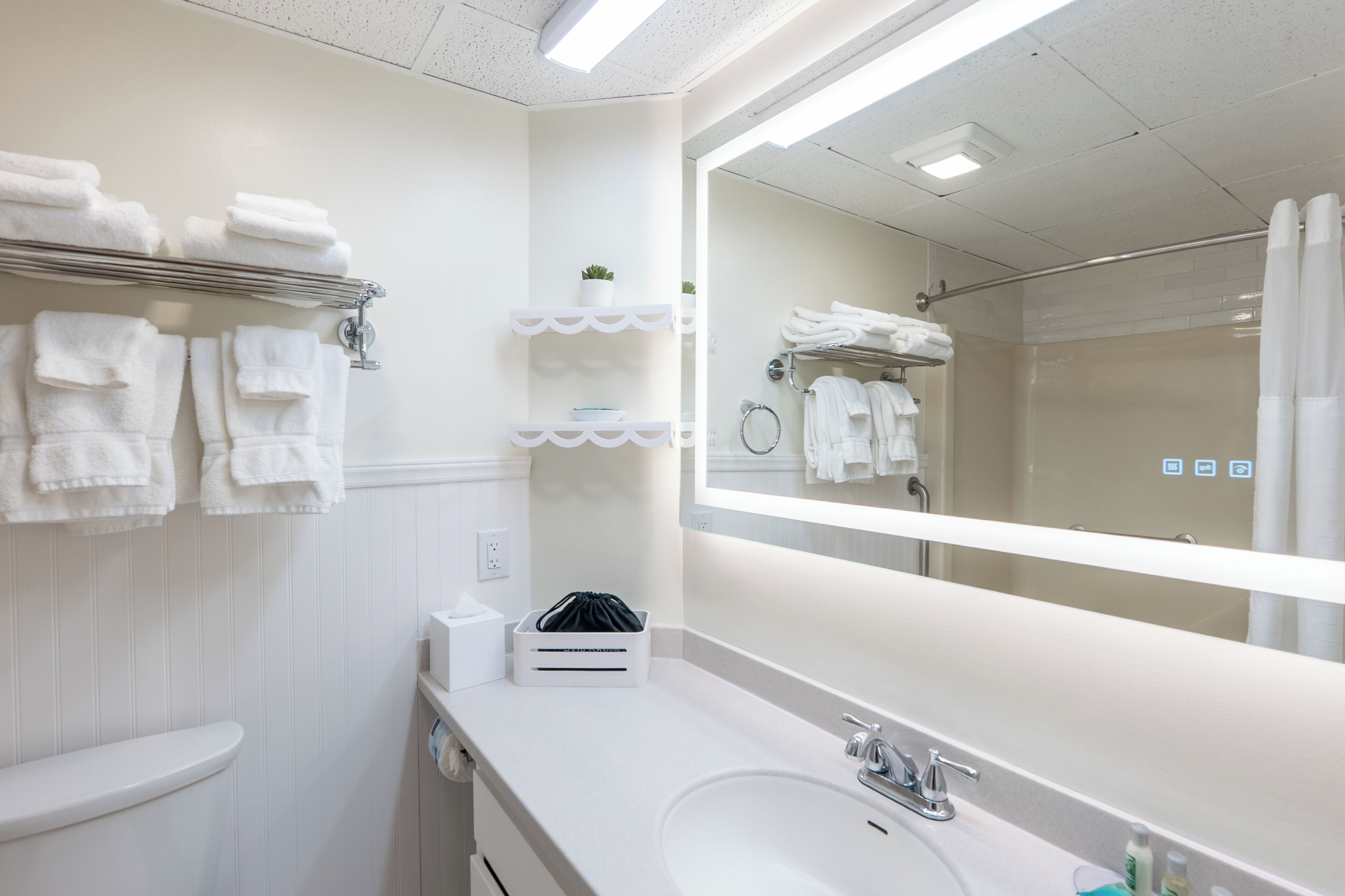 Un bagno moderno con uno specchio grande, asciugamani bianchi su scaffali, un lavandino e una zona doccia.