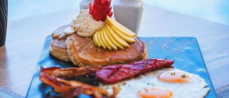A breakfast plate with pancakes, eggs, bacon, and fruit on a blue plate.
