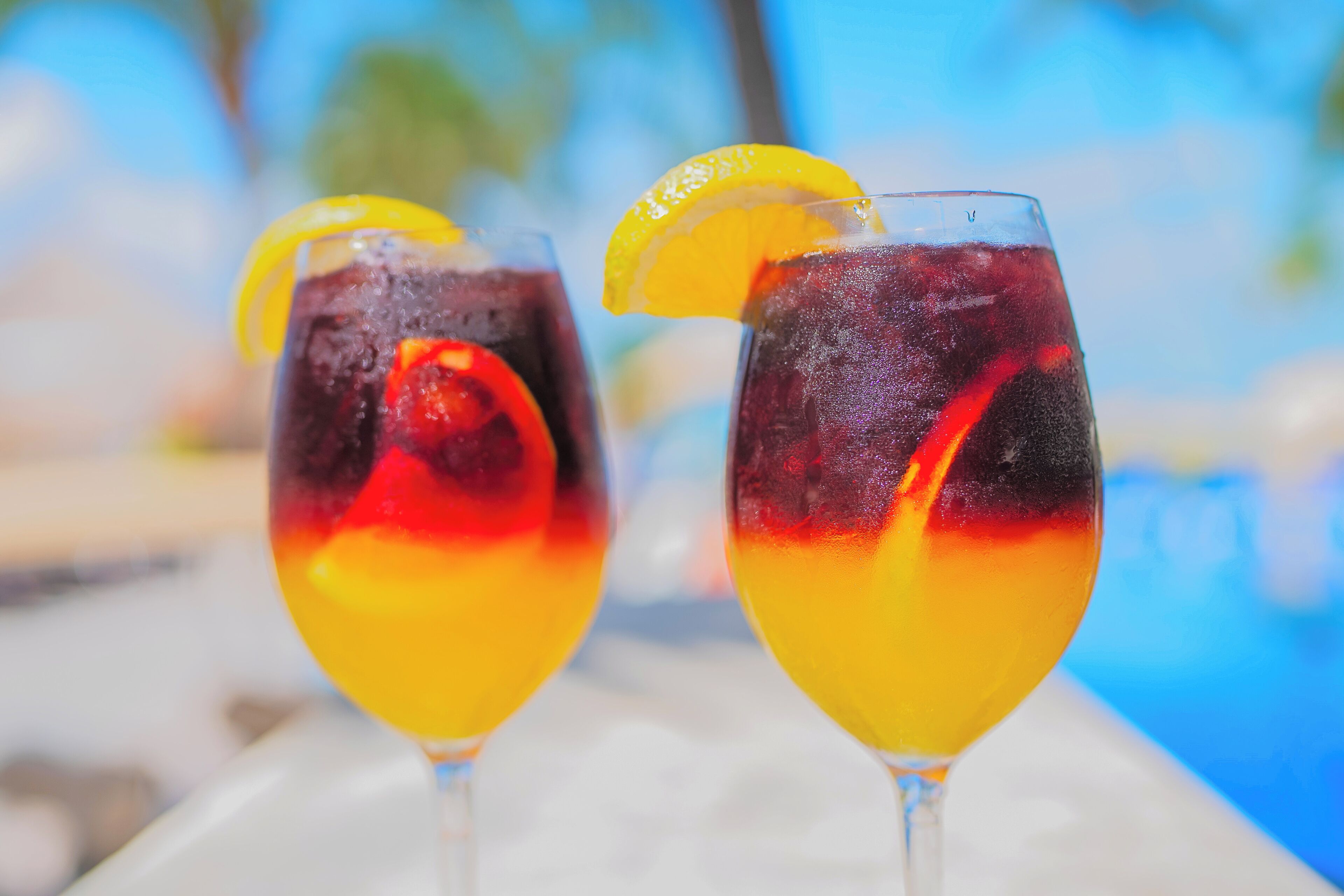 Two glasses of a layered beverage with a slice of orange on the rim, placed on a surface with a blurred background.