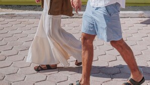 A couple walking on a paved path with a yellow building featuring blue window frames in the background.