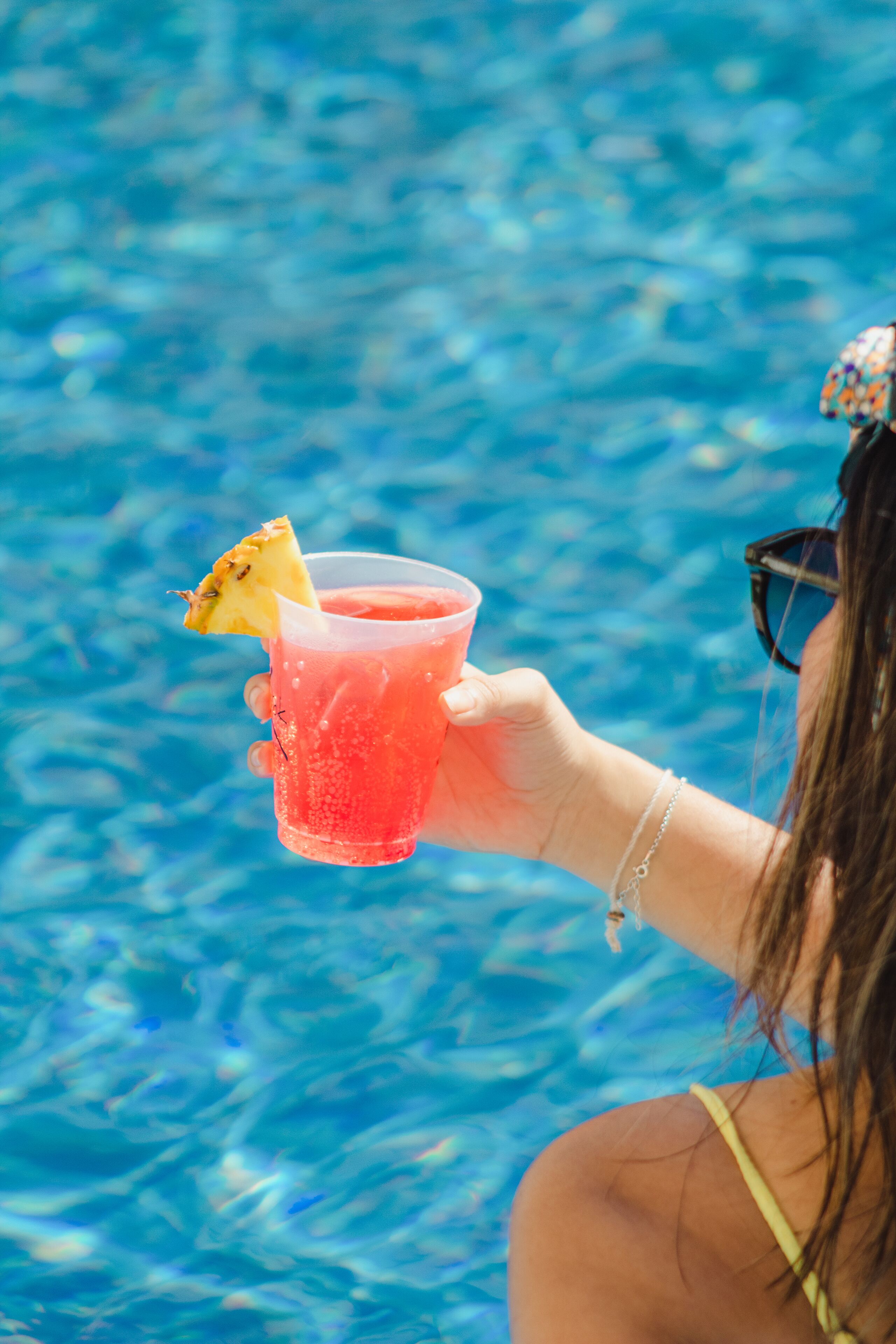 Una persona sosteniendo una bebida con una rodaja de piña en una piscina.