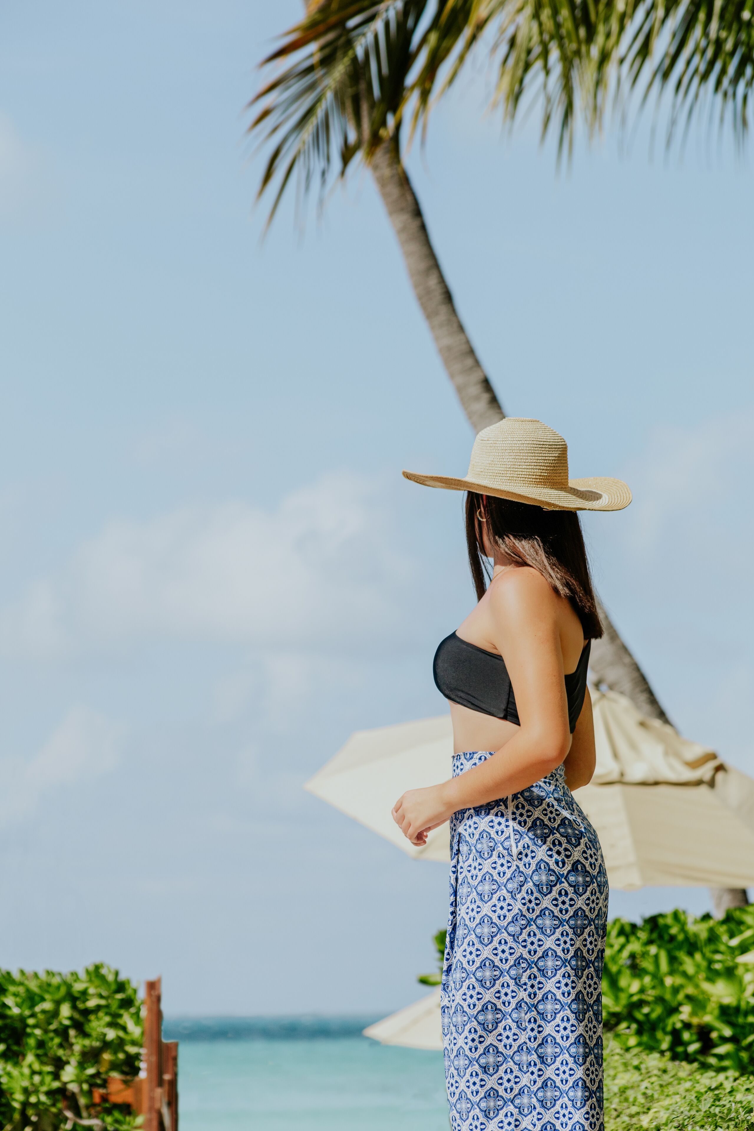 A person standing by a pool with a palm tree and a beach umbrella in the background.