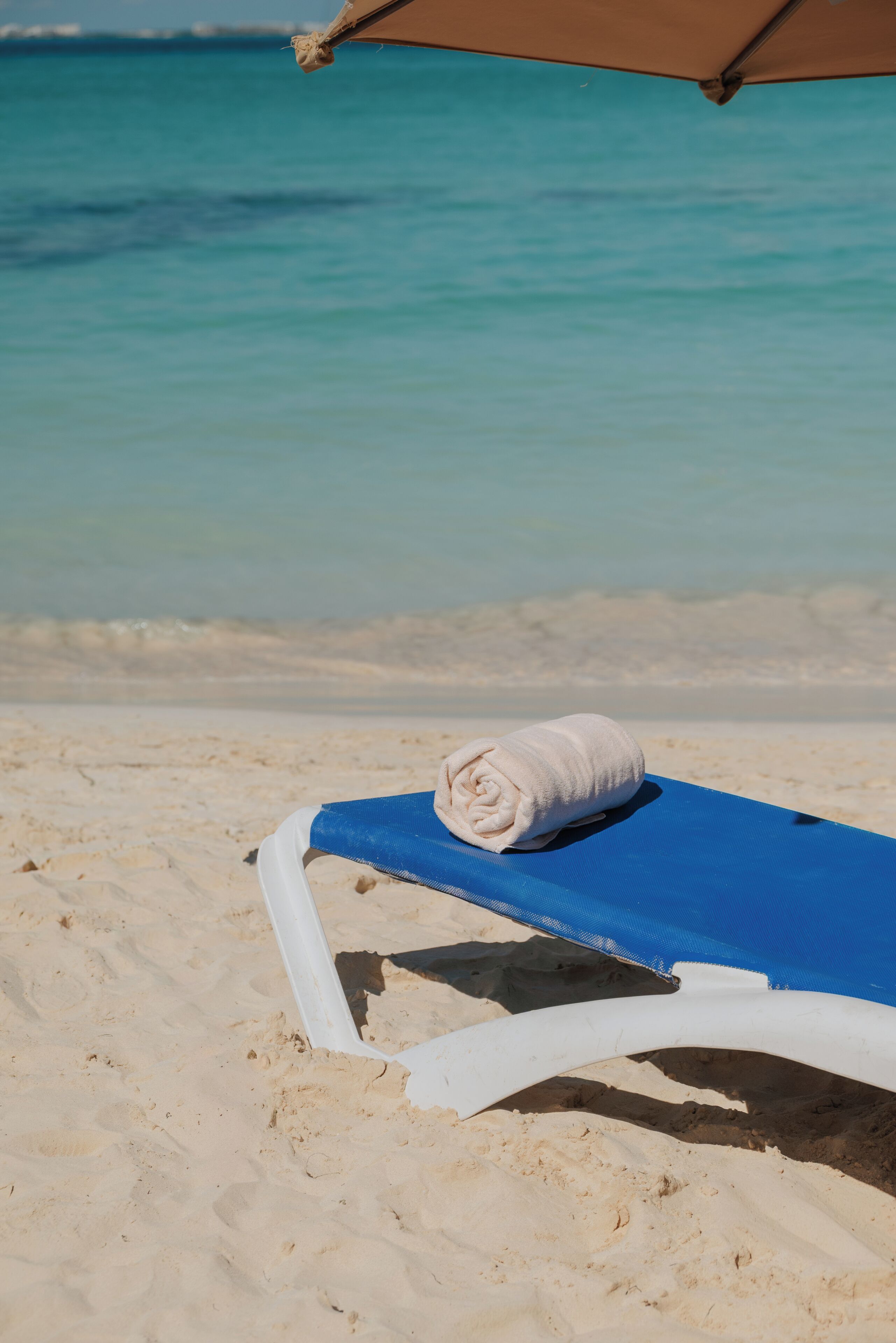 A beach chair with a towel, a blue sunshade, and a view of the ocean.
