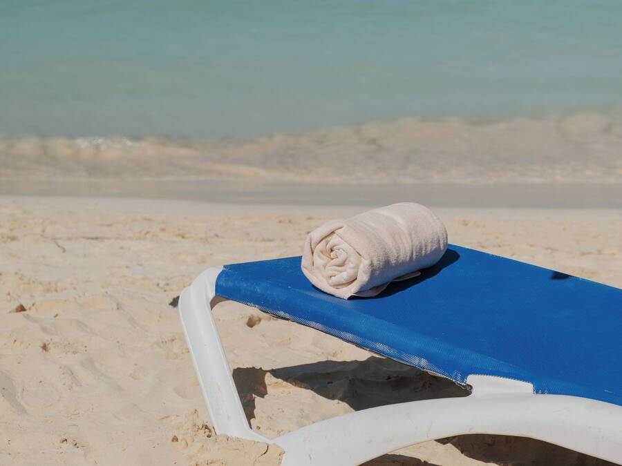 A beach chair with a towel, a blue sunshade, and a view of the ocean.