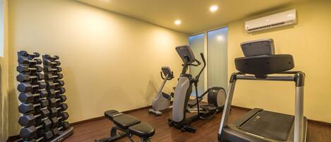 A home gym with a treadmill, elliptical, dumbbells, and a bench.