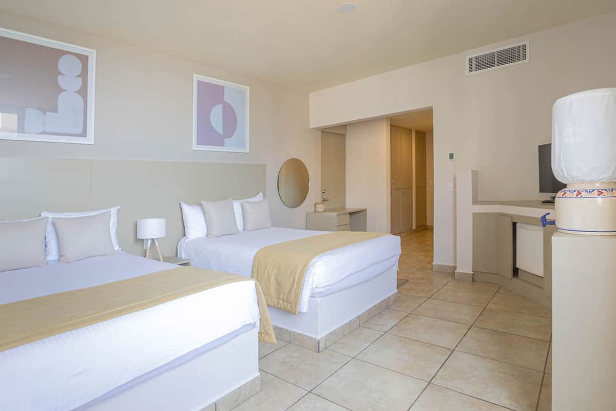 A hotel room with two beds, a desk, a mirror, and a television.