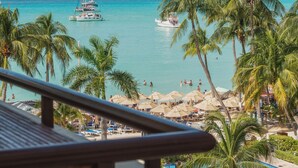 A beach view with palm trees, a pool, and a boat in the water.