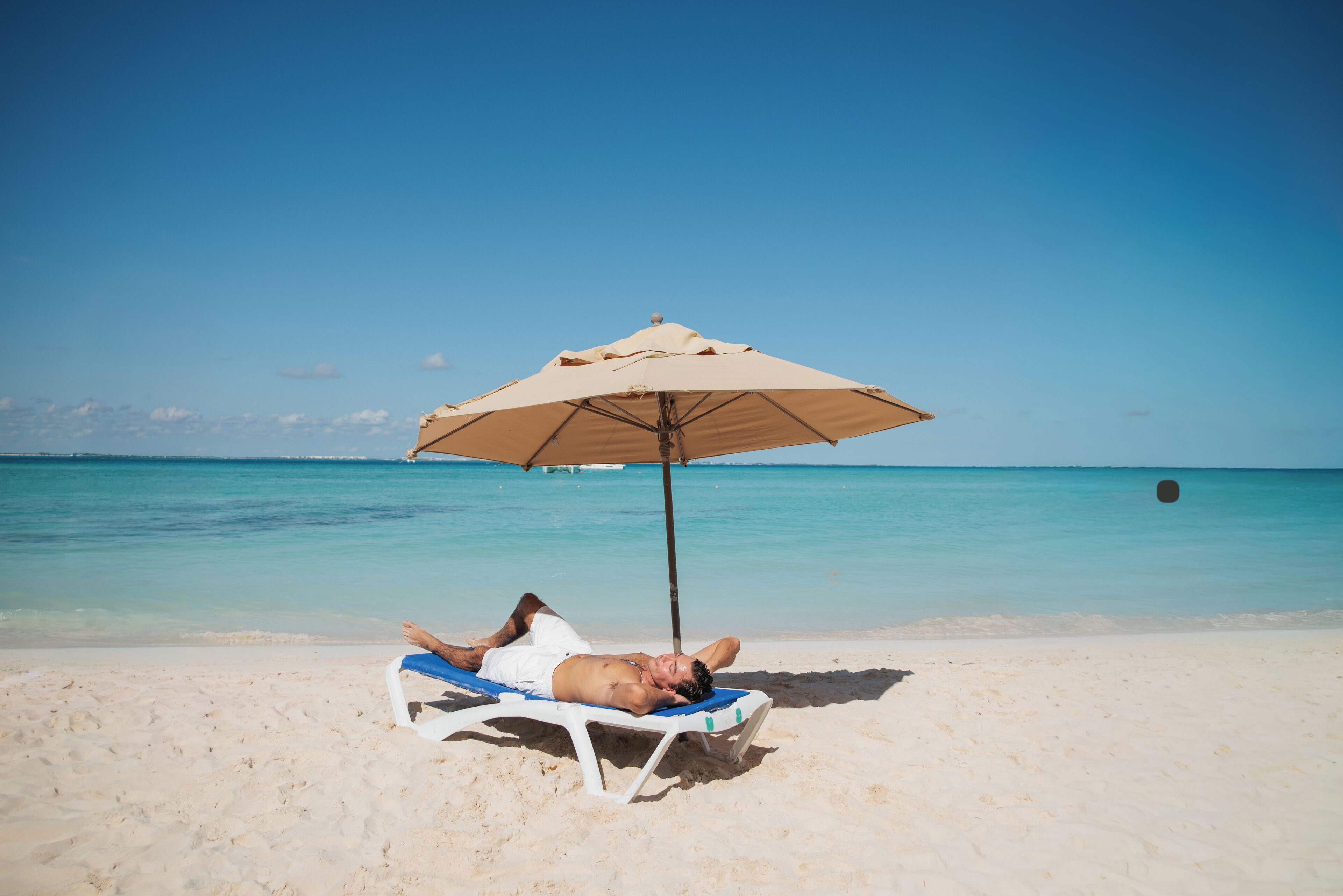 Iemand ligt op een strandstoel onder een strandparasol.