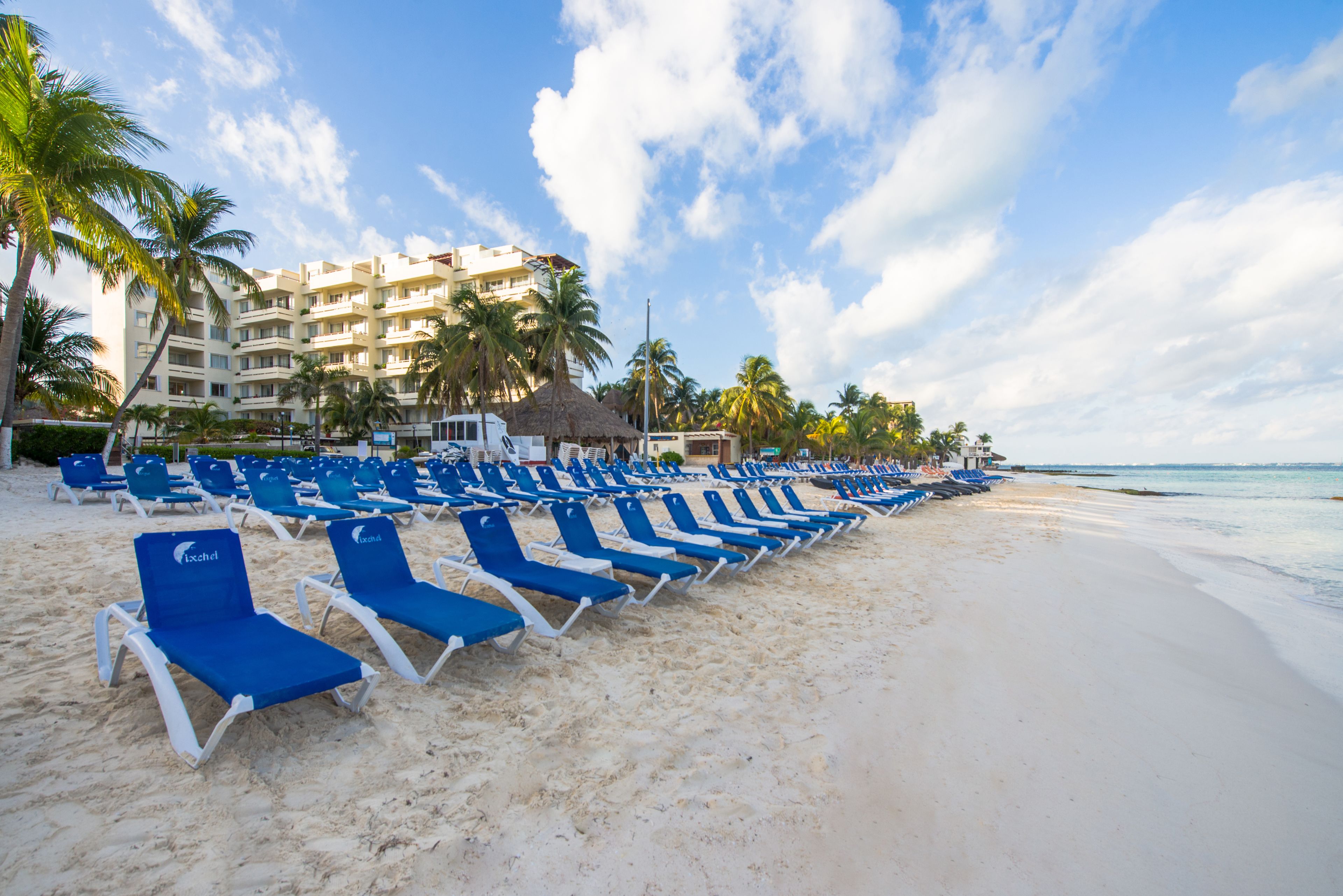 A beach with rows of blue lounge chairs and a hotel in the background.