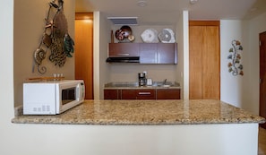 A kitchen with granite countertops, a white microwave, a coffee maker, and decorative wall art.