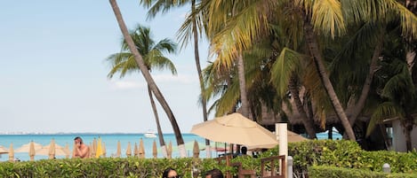 A poolside area with lounge chairs, palm trees, and a view of the ocean.