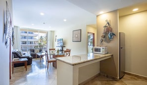 A modern kitchen with a central island, a dining area with a sofa and chairs, and a view of a building with balconies.