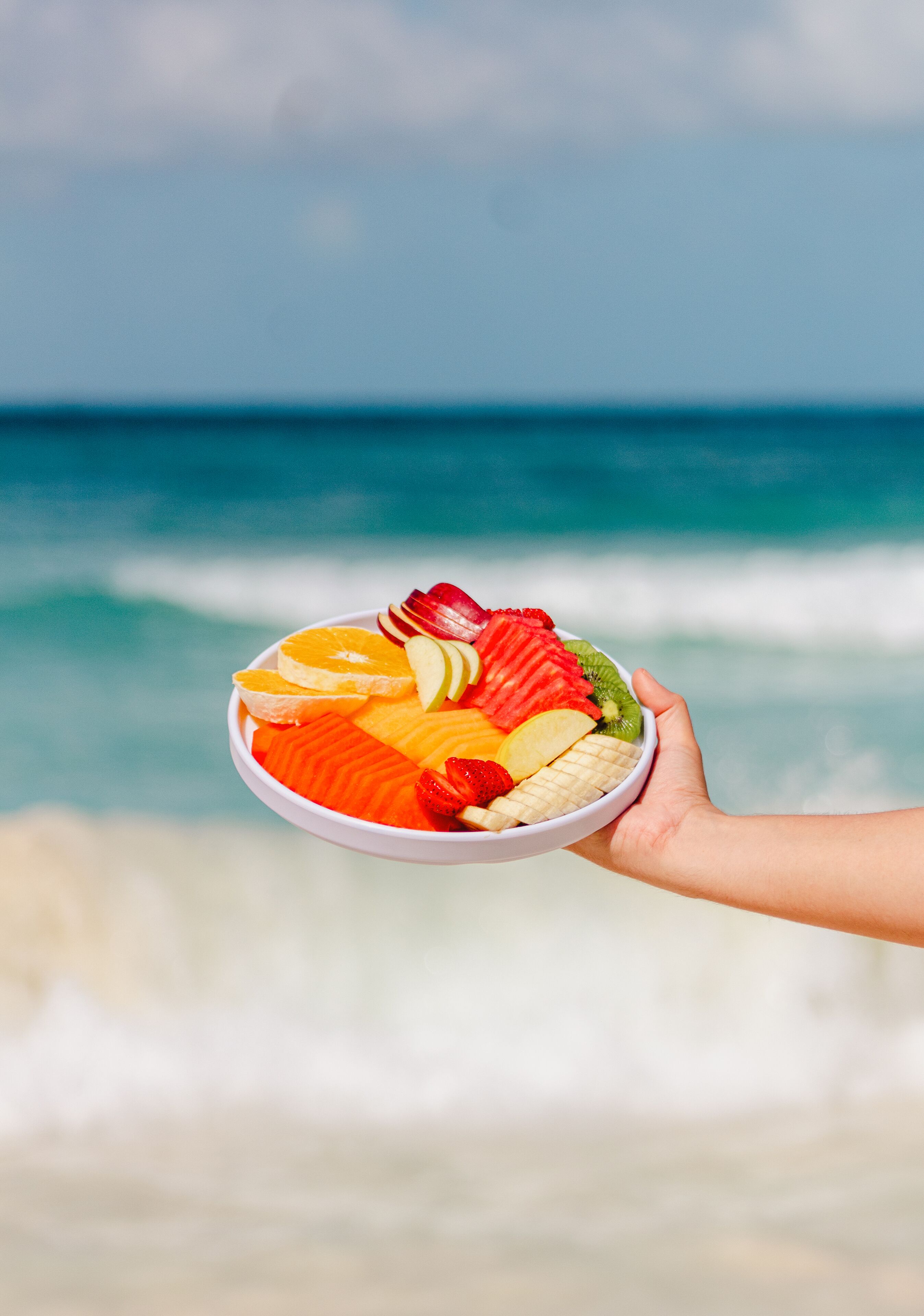 Uma tigela de frutas suspensa sobre uma praia, com ondas ao fundo.