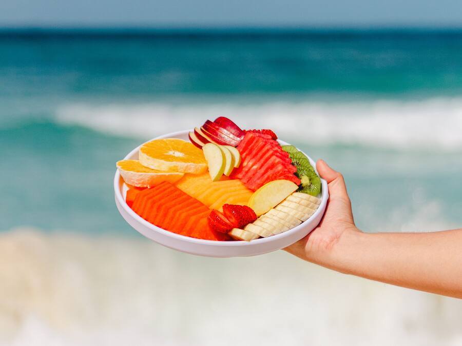 Een schaal fruit boven een strand, met golven op de achtergrond.