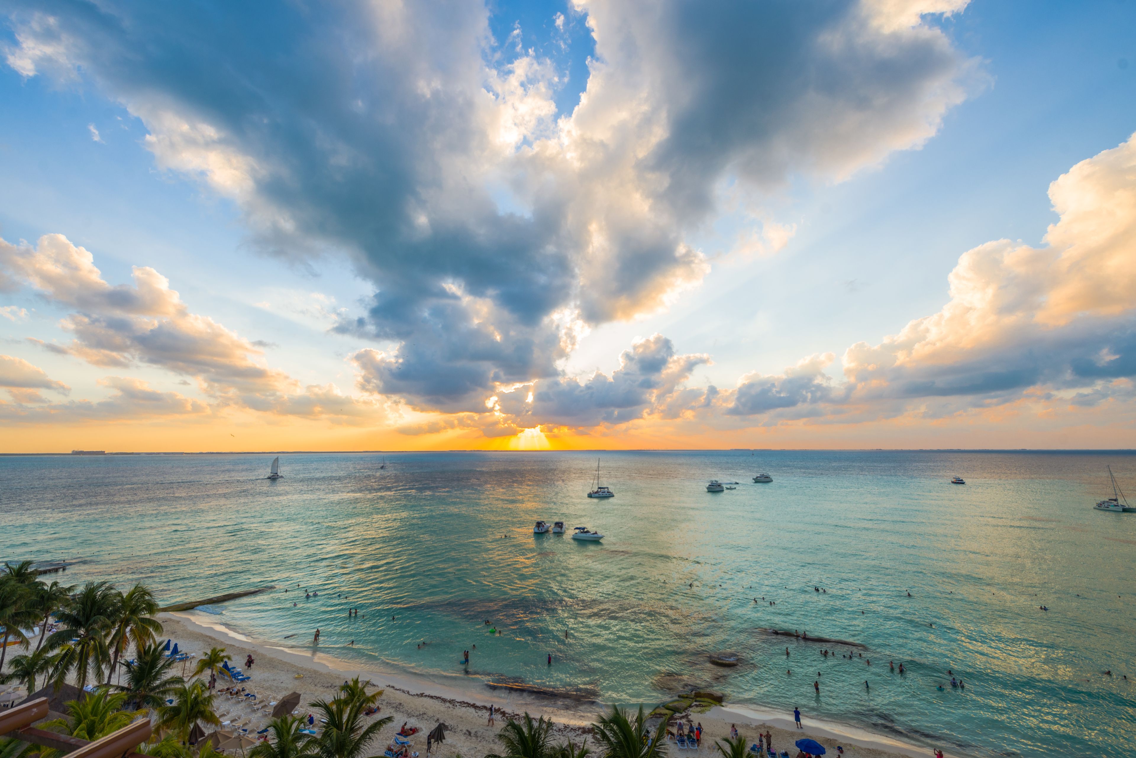 Una playa con aguas turquesas cristalinas, barcos y una puesta de sol.