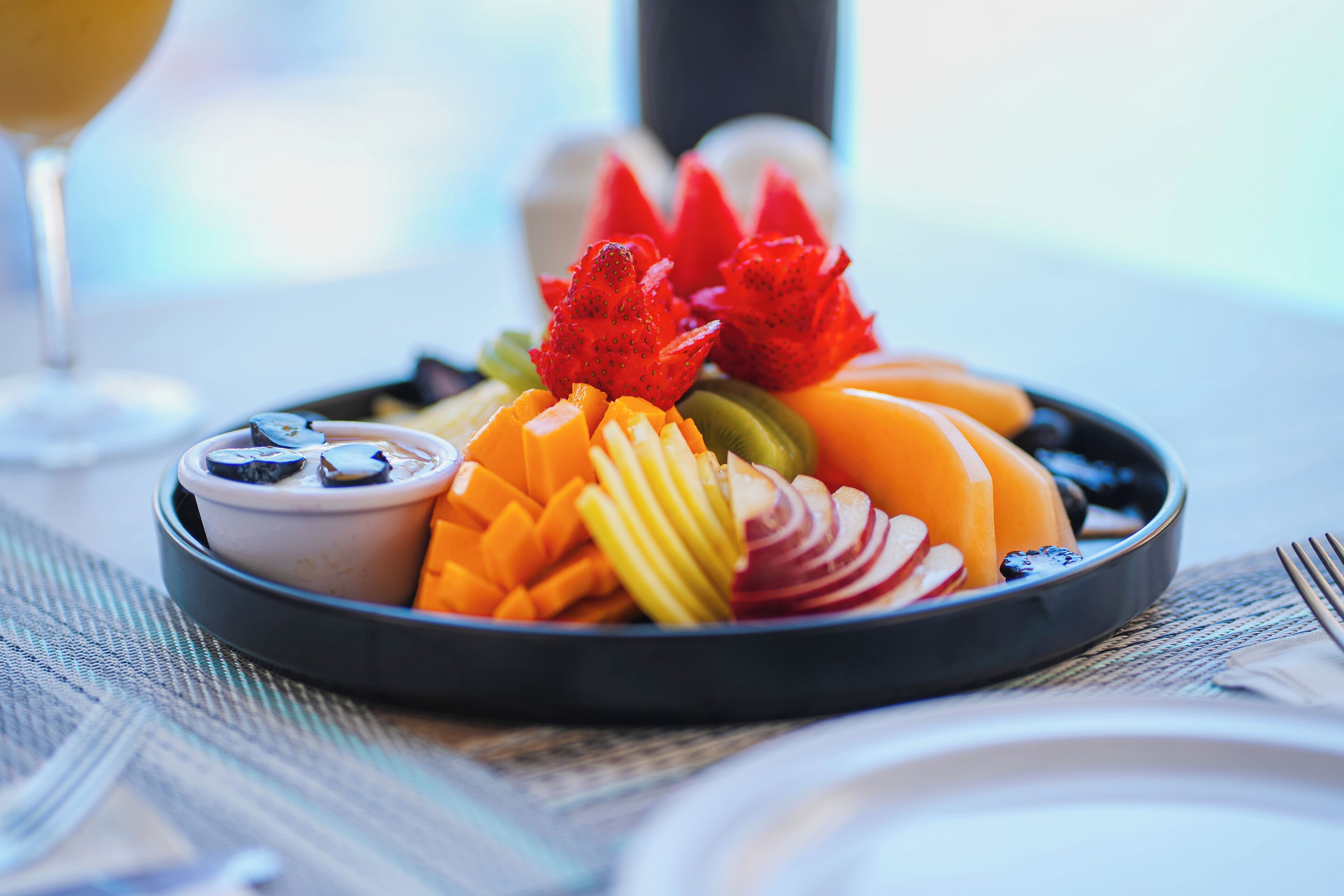 A fruit platter on a table with a glass of wine in the background.