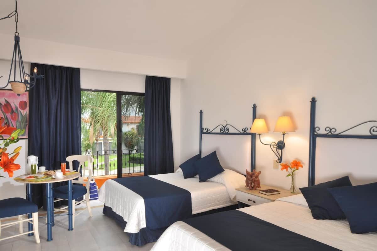 A hotel room with two beds, a dining table, and a balcony with curtains.