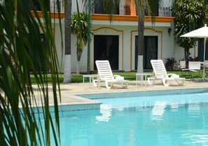 A swimming pool with lounge chairs and a building with a balcony.