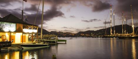 A marina at dusk with boats docked, a building with a sign, and a bridge in the background.